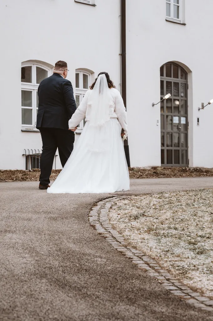 Der gemeinsame Weg in die Zukunft Brautpaar geht Hand in Hand einen Weg entlang, vom Fotografen abgewandt. Natürliches Paarshooting im Freien nach der Hochzeit.