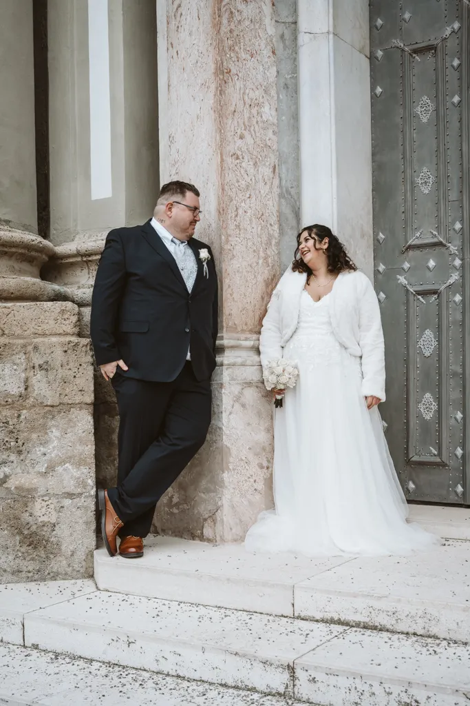 Modernes Paarshooting in historischer Kulisse Lässiges Brautpaar-Porträt am Kloster Fürstenfeld: Braut und Bräutigam lehnen entspannt an einer historischen Mauer und halten Blickkontakt.