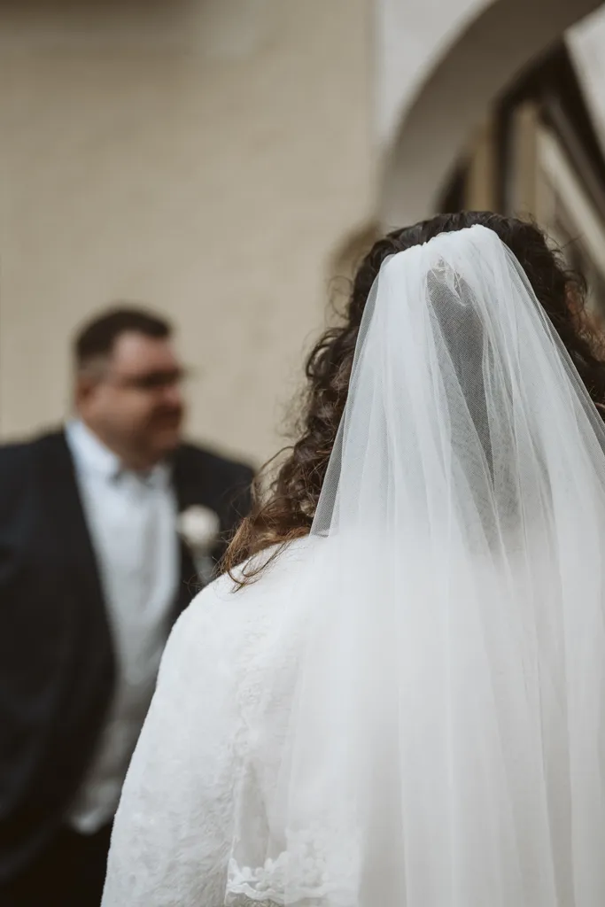 Emotionales Brautpaar-Shooting Künstlerische Hochzeitsfotografie: Nahaufnahme des Brautschleiers von hinten mit dem Bräutigam im unscharfen Hintergrund (Bokeh).