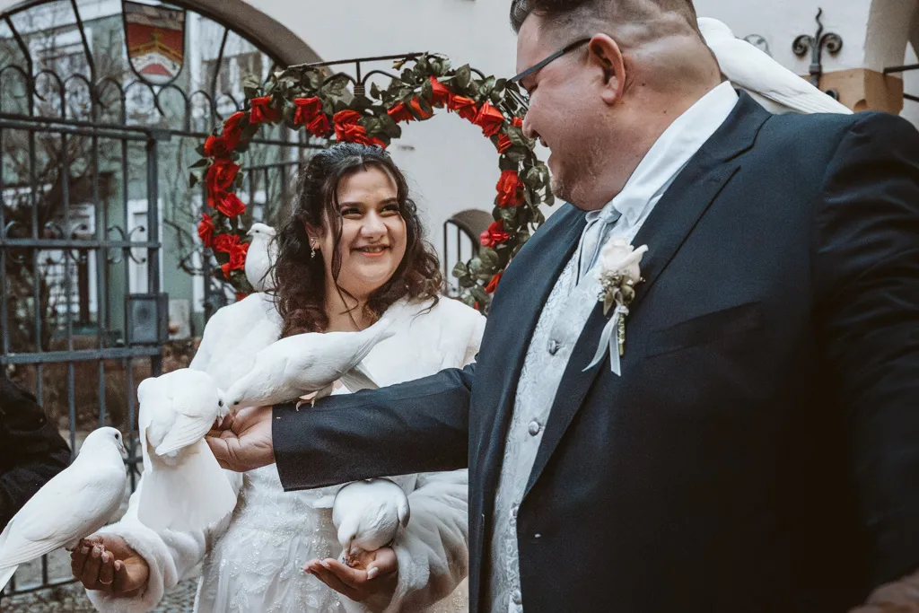Gemeinsames Füttern der weißen Hochzeitstauben Brautpaar füttert gemeinsam weiße Hochzeitstauben nach der Trauung in Fürstenfeldbruck. Emotionales Porträt der Hochzeitsbegleitung.