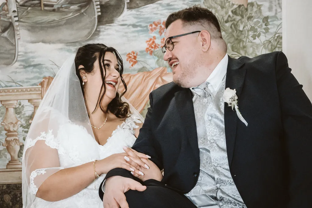 Ein gelöster Moment auf den Stufen Entspanntes Brautpaar-Porträt: Braut und Bräutigam sitzen lachend auf einer Treppe und schauen sich tief in die Augen.