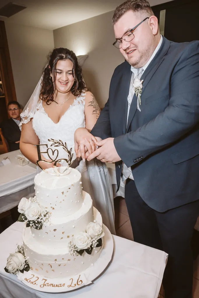 Der feierliche Anschnitt der Hochzeitstorte Das frisch verheiratete Ehepaar schneidet gemeinsam die mehrstöckige Hochzeitstorte an. Fröhliche Stimmung während der Hochzeitsfeier.