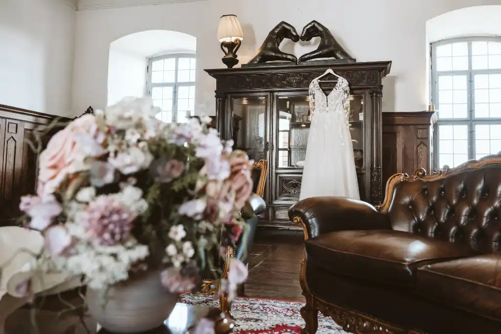 Brautkleid im Schlossraum am Schrank Brautkleid hängt an einem Holzschrank in einem prächtigen Schlossraum