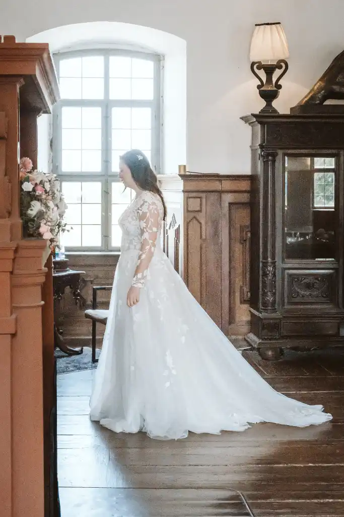 Getting Ready – Braut von der Seite am Fenster Braut im Brautkleid steht im Profil vor einem großen Fenster beim Getting Ready im Schloss