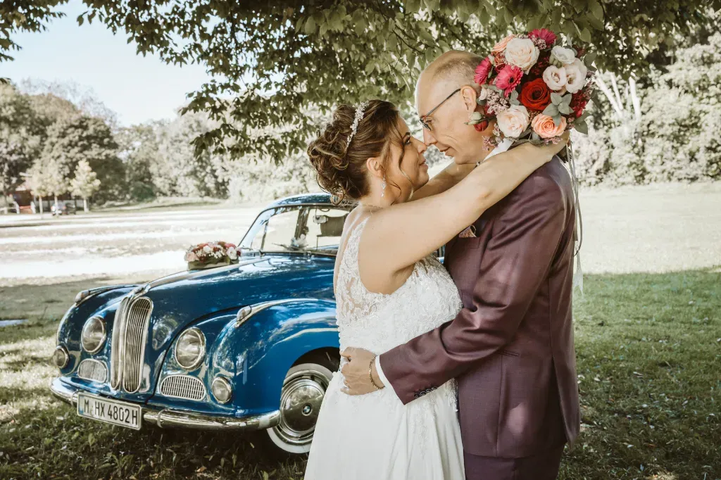 Innige Umarmung mit Brautstrauß Brautpaar-Shooting Olching: Die Braut umarmt den Bräutigam liebevoll. Der Brautstrauß ist während der Umarmung im Hintergrund hinter dem Kopf des Bräutigams platziert.