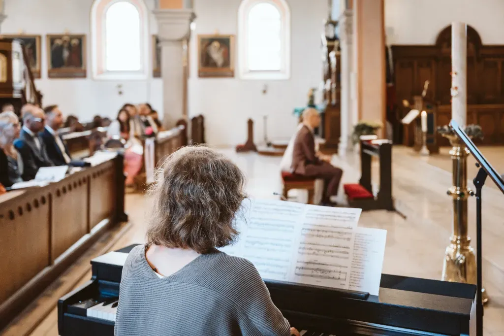 Klavierbegleitung während der Trauung in Olching Hochzeitsfotograf Olching: Stimmungsvolle Aufnahme des Klaviers, das die Hochzeitszeremonie in der Kirche begleitet. Im Hintergrund ist das Brautpaar
