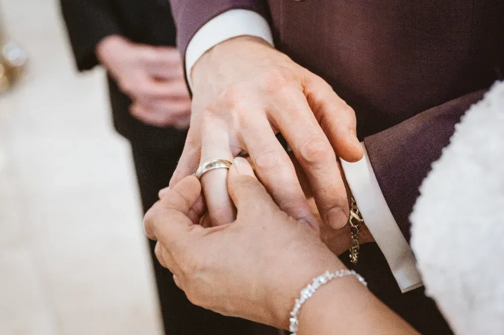 Detail: Anstecken der Eheringe bei der Trauung Hochzeitsbilder Olching: Detailaufnahme der Hände beim Anstecken der Eheringe während des Ringtausches in der Kirche. Ein intimer Moment, festgehalten vom Wedding Photographer aus Olching.