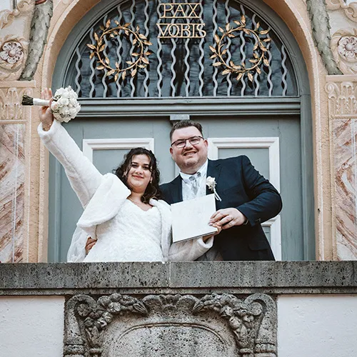 Hochzeitsfotograf aus Olching fotografiert Brautpaar auf dem Balkon des Rathauses Fürstenfeldbruck beim Winken nach der Trauung.