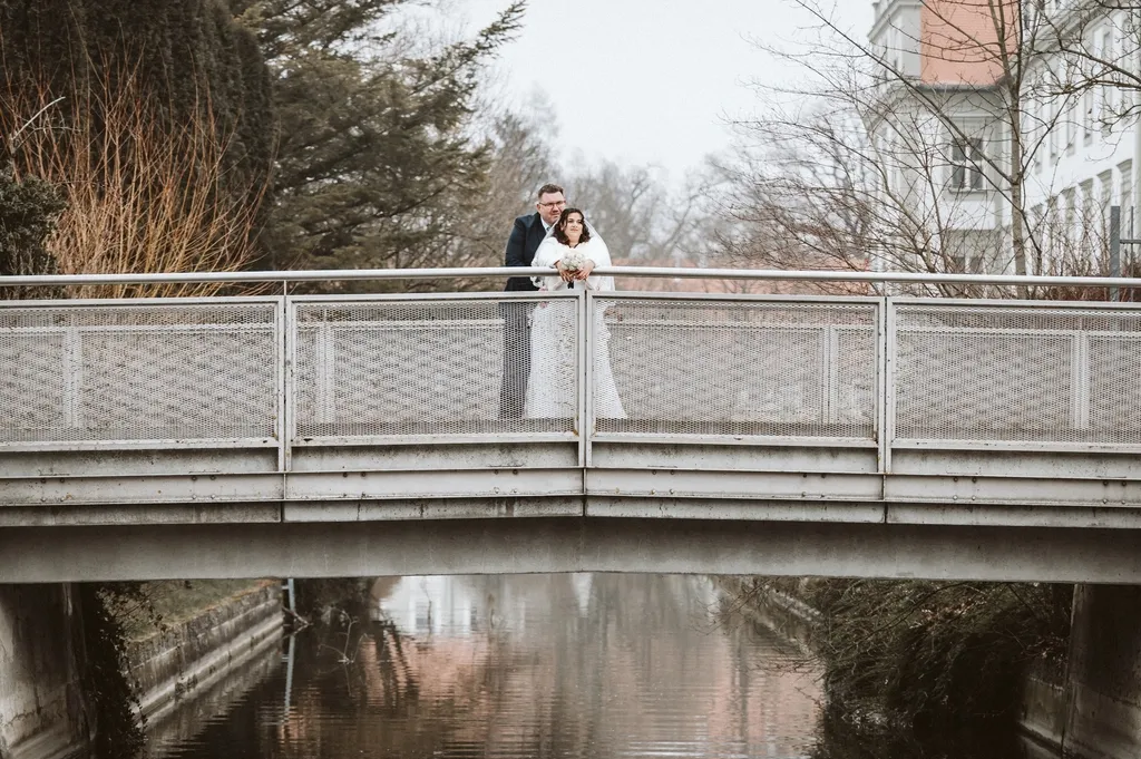 Romantisches Brautpaar-Shooting auf einer Brücke am Kloster Fürstenfeld: Innige Umarmung des Paares, festgehalten von einem Hochzeitsfotografen aus Olching.
