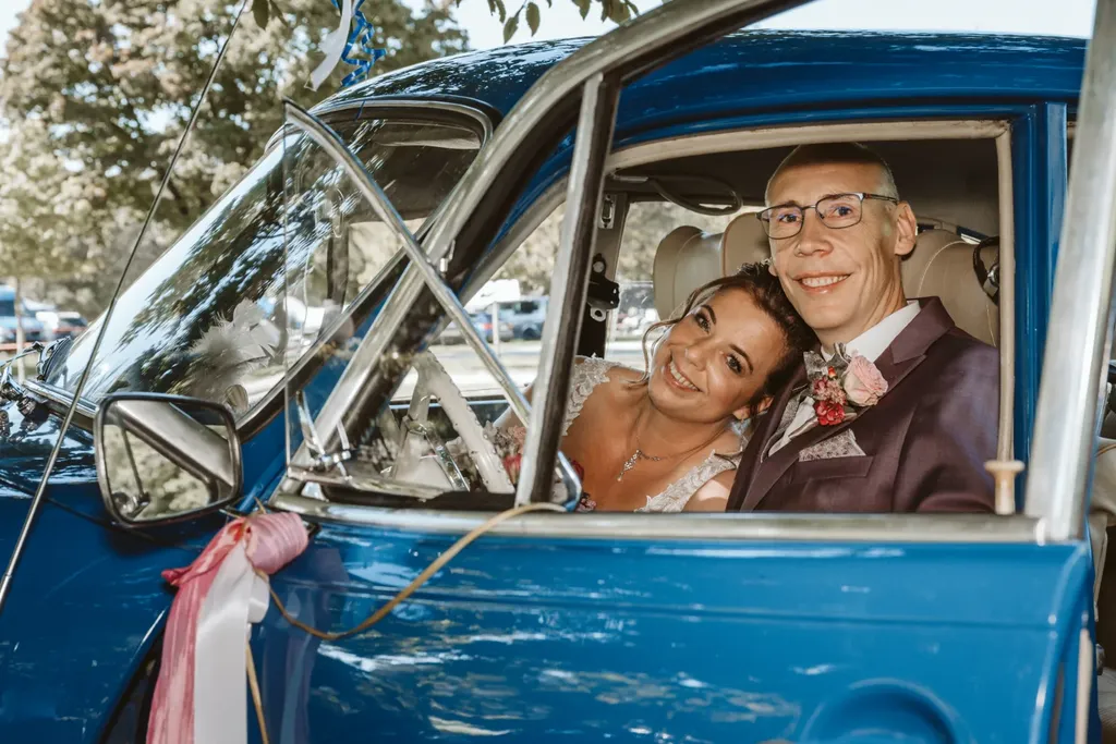 Das lachende Brautpaar Nicole und Manfred im Hochzeitsfahrzeug, sie hat ihren Kopf entspannt an seine Schulter gelehnt und blickt zu mir. Eine authentische Momentaufnahme, die ich als Ihr Hochzeitsfotograf Olching eingefangen habe.