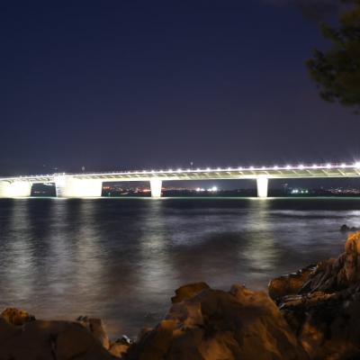Nachtaufnahme in Langzeit. Das Meer wirkt eingefrohren. Die Brücke wird mit weißen Lampen beleuchtet.