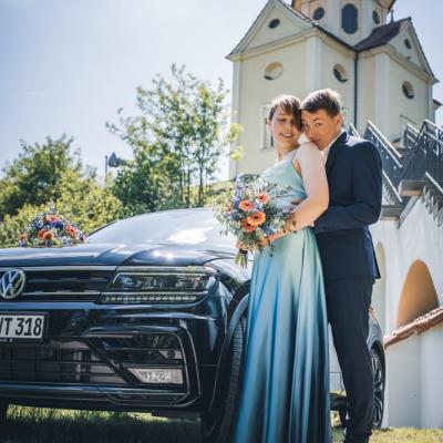 Das frisch verheiratete Paar strahlt vor Glück, als es neben seinem Hochzeitsfahrzeug posiert.